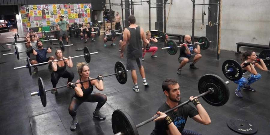 Grupo de atletas praticando back squats em uma aula de CrossFit, focando em força e técnica.
