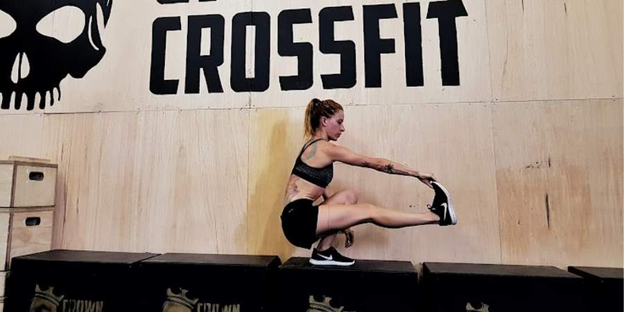 Uma atleta feminina de CrossFit executa um pistol squat com técnica aprimorada em frente a um grande logotipo de CrossFit, enfatizando o poder do treinamento funcional e a importância da forma física.