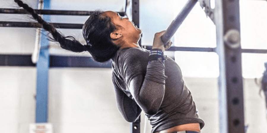 Atleta feminina com longa trança realizando pull-ups em uma barra de ginástica, exibindo força e determinação em sua sessão de treino de CrossFit.