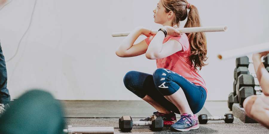 Mulher usando PVC para aprender squat snatch em um box de CrossFit.