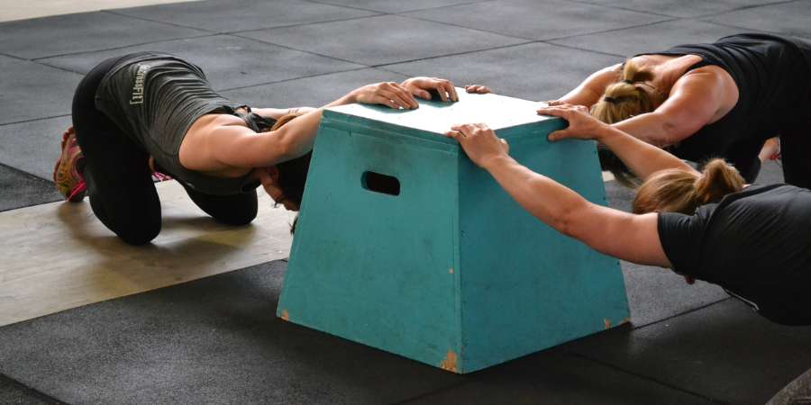 Três mulheres fazendo alongamento no CrossFit usando uma box de apoio para os braços.
