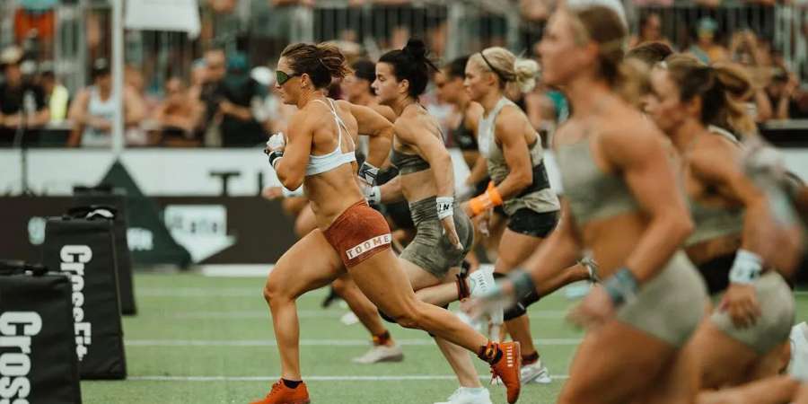 Um grupo de atletas femininas em uma corrida durante uma competição de CrossFit, demonstrando velocidade e resistência, com uma líder evidente, todas focadas e determinadas, simbolizando a competição saudável e o esforço máximo característicos de um treino AMRAP.