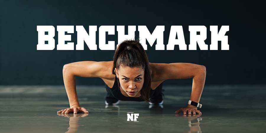 Uma atleta concentrada fazendo flexões, com a palavra "BENCHMARK" em destaque, simbolizando o teste de desempenho e força em treinos de CrossFit.
