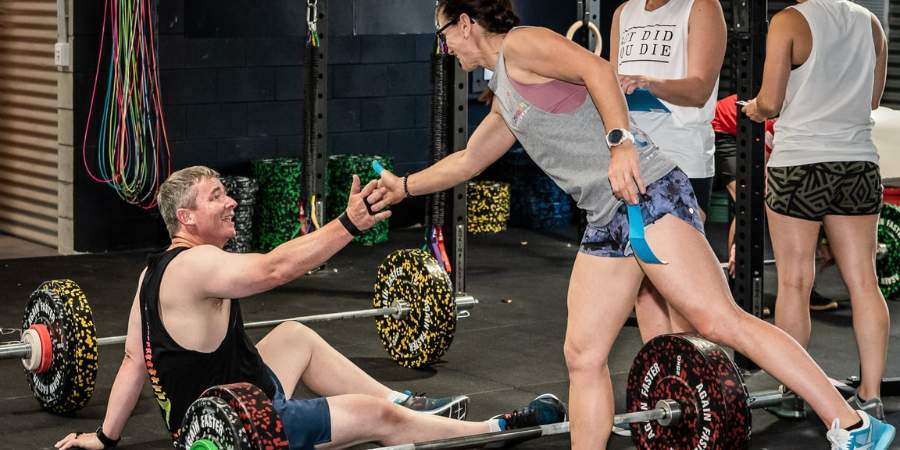Mulher comprimentando parceiro de treino que esta sentado no chão em uma box de CrossFit.