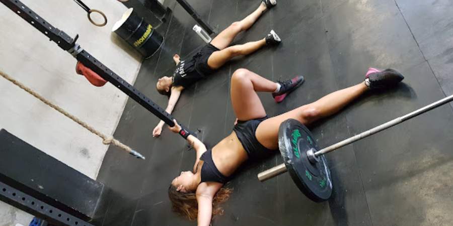 Duas mulheres deitadas e cansadas pós treino de CrossFit.